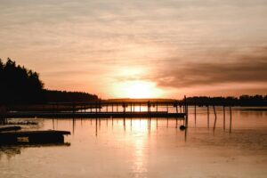 Tässä kuvassa nähdään upea auringonlasku vesireunan luona. Aurinkoa heijastuu rauhalliseen veteen, ja varjoinen puisto reunustaa maisemia. Ranta-alta rakenteita, jotka nostavat tunnelman. TikTok: Kuinka tavoittaa nuoret suomalaiset – löydä inspiraatiota tällaisista kauniista paikoista ja kerro heille tarinoita, jotka kiinnostavat nuoren sukupolven.