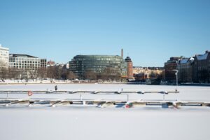 Tässä kuvassa on luminen lahti tai vesipiiri, jonka varrella on rakennuksia, mukaan lukien ympyräinen lasirakenne. Jotkut ihmiset kävelevät varrelta, ja luminen maisema antaa rauhallisen tunnelman. YouTube -videomarkkinoinnissa Suomessa on suuria mahdollisuuksia. Tällaiset maisemat voivat olla osa videomerkinnöjä, jotka vaikuttavat kansalaisiin, kiinnostamalla heidät tutustumaan entistä enemmän Suomen luontoon ja kaupunkiin.